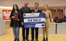 Przedstawiciele samorządu, burmistrz oraz marszałek z tablicą prezentującą kwotę dofinansowania