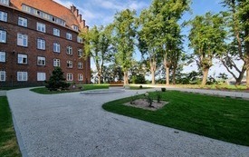 Skwer im. Joannit&oacute;w z kamieniem z nazwą i budynkiem w tle