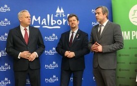 Wiceminister Aktyw&oacute;w Państwowych, Burmistrz Miasta Malborka oraz Wiceprzewodniczący Rady Miasta Malborka stoją na tle baneru z napisami MALBORK