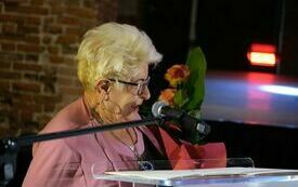 Starsza kobieta z kwiatami przemawia do mikrofonu