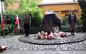 Pomnik Żołnierzy AK z kwiatami, po obu stronach harcerz