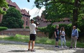 kobieta i mężczyzna prowadzący program telewizyjny rozmawiają z pracownikiem Muzeum Zamkowego, na pierwszym planie kamerzysta