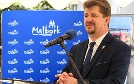 Burmistrz Miasta Malborka Marek Charzewski w tle ścianka z logotypem miasta Malbork