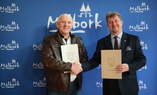 wykonawca z burmistrzem na tle ściance z napisem Malbork