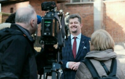 Burmistrz Marek Charzewski udziela wywiadu, na pierwszym planie kamera telewizyjna i tłumacz